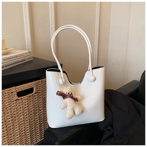 White faux leather tote bag with cute plush bear charm on a stylish side table