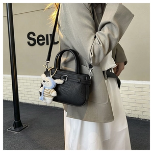 Close-up of black litchi pattern leather handbag with silver hardware and a cute bear charm