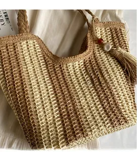 Détail d'un sac cabas en paille tissée avec motif à carreaux marron et breloque à pompon