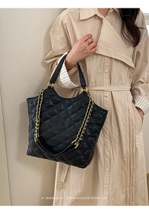 Detail of black quilted tote bag with gold chain strap on model in trench coat