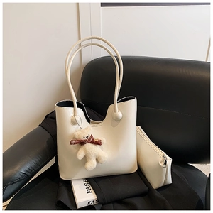 Detail of cream tote bag set with matching pouch and plush bear charm on black leather