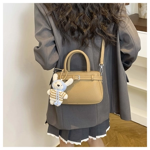 Detail of khaki pebbled leather handbag with rabbit plush pendant and crossbody strap
