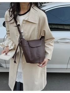 Close-up of a dark brown lychee pattern leather bucket bag held by a model in a beige coat