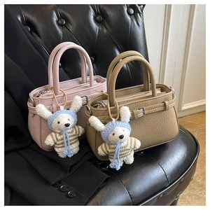 Detail of pink and khaki pebbled leather handbags with cute bunny charms on black chair