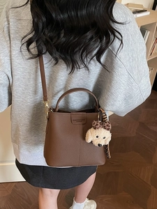 Brown litchi grain leather bucket bag with dog charm and adjustable shoulder strap