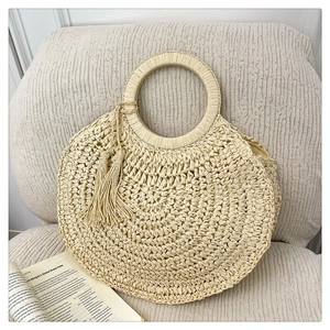 Détail du sac rond en paille tissé à la main avec pompons bohèmes et poignée circulaire