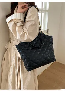 Detail of black quilted tote bag with golden chain strap on model in minimalist interior