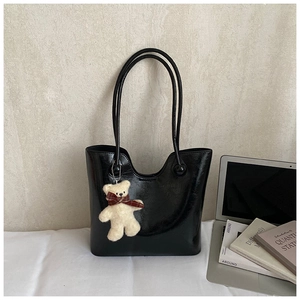 Detail of black glossy tote bag with cute plush bear charm and textured PU leather