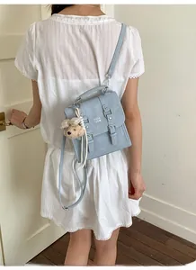 Close-up of a light blue rectangular crossbody bag with dual buckles and bear charm
