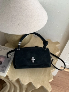 Modern black suede crossbody bag with silver twist lock on elegant wavy surface
