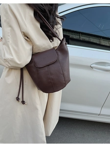 Detail of dark brown leather bucket bag with litchi texture and elegant drawstring strap