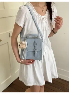 Close-up of light blue frosted leather handbag with double buckles and a plush bear charm