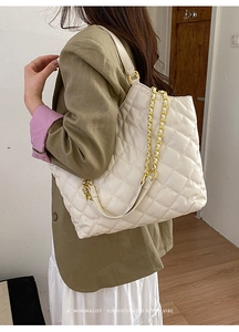 Close-up of white quilted tote bag with golden chain straps worn by a model in a studio