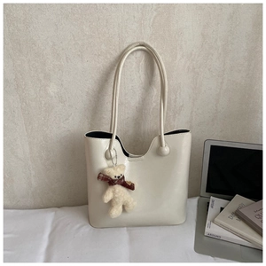Detail of cream tote bag with wave edge design and cute plush bear charm on a desk