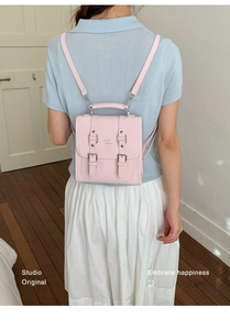 Detail of pink mini backpack featuring silver metal buckles and top handle on a model
