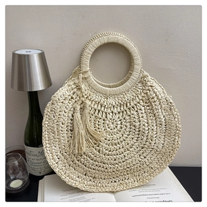 Détail d'un sac cabas en paille tissée avec poignée ronde et pompons de style bohème