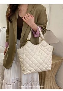 Detail of quilted diamond pattern and gold metal buckle on cream tote bag