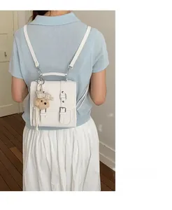 White leather square backpack with decorative straps and a plush bear pendant on model