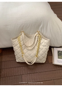 Detail of off-white quilted tote bag with golden metal chain strap on wooden floor