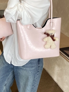 Pale pink glossy tote bag with teddy bear charm shown worn on a shoulder