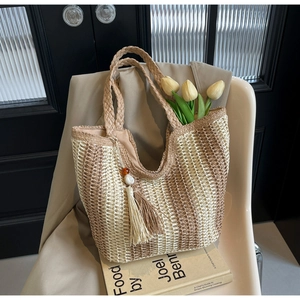 Détail d'un sac cabas en paille tissée avec rayures verticales et pompons décoratifs