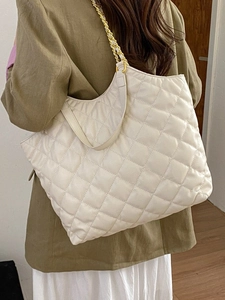 White quilted tote bag with gold chain strap shown on model for high capacity and style