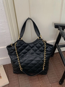 Quilted black leather tote bag with gold chain strap shown in a lifestyle interior