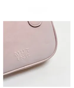Détail d'un sac à main en cuir rose clair avec le logo MUTING embossé sur le côté