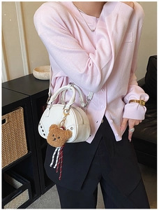 Lifestyle view of a white shell handbag with silver studs and cute bear charm