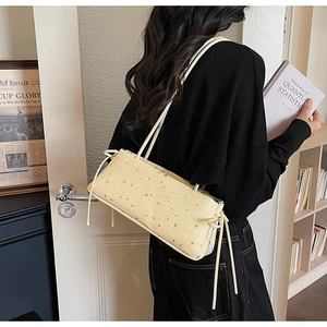 Detail view of cream star-print underarm bag with decorative tassels in a cozy home setting