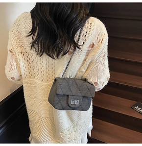 Detail of dark grey quilted chain crossbody bag with silver lock on a knit sweater