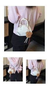 Close-up of white shell bag with metal studs, logo print, and a brown plush bear charm
