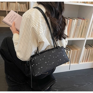 Detail of black crossbody bag with white star print worn by model by a bookshelf