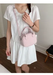 Petit sac à main rose pâle en cuir mat porté par un mannequin avec bandoulière réglable