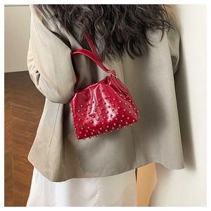 Detail of red crossbody bag featuring studded base and pleated top with shoulder strap