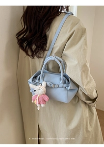 Détail du sac seau en cuir bleu clair avec breloque lapin sur un trench-coat beige chic