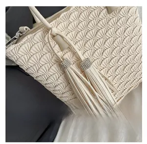 Détail du sac à pompon crème avec texture plissée et garniture métallique sertie de strass