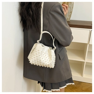 Detail of white leather bucket bag with dense pearl embellishments and a crossbody strap