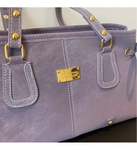 Macro shot of purple leather tote bag showing white contrast stitching and gold metal plate