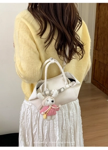 Détail du sac seau en cuir blanc avec un charmant lapin en peluche rose sur la poignée