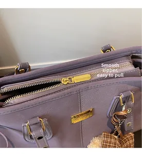 Close-up of purple leather tote featuring a golden zipper and a plaid bow charm detail