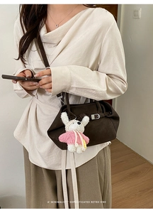 Détail d'un sac bandoulière rétro marron foncé avec un joli pendentif lapin blanc