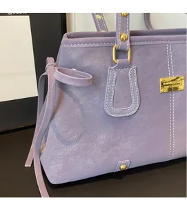 Detail of lilac leather tote bag featuring white contrast stitching and gold logo plaque