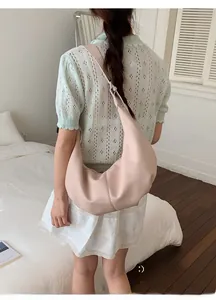 Minimalistische sichelförmige Schultertasche aus Leder in Pastellrosa, getragen von Model