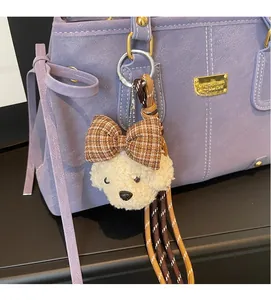 Detail of white plush puppy bag charm with brown plaid bow on a purple leather tote bag