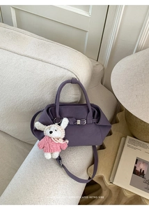 Détail du sac seau en cuir violet avec boucle et breloque lapin posé sur un canapé