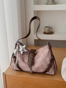 Pink suede underarm bag with star charm on wooden shelf in soft natural light