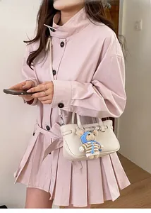 Detail einer beigen Lederhandtasche mit Kieselstruktur und süßem Bärenpuppen-Anhänger