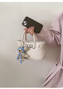Detail der cremefarbenen Ledertasche mit Silberverschluss und blauem Bärenanhänger