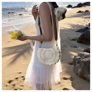 Close-up of beige crochet shoulder bag with intricate woven patterns on a beach background